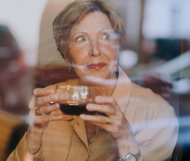 Ältere Dame sitzt in einem Café und ist dankbar für ihre abgeschlossene Ablebensversicherung.