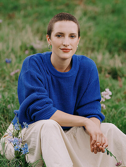 Junge Dame mit kurzer Frisur sitzt auf einer Blumenwiese und steht für die Krebsversicherung.