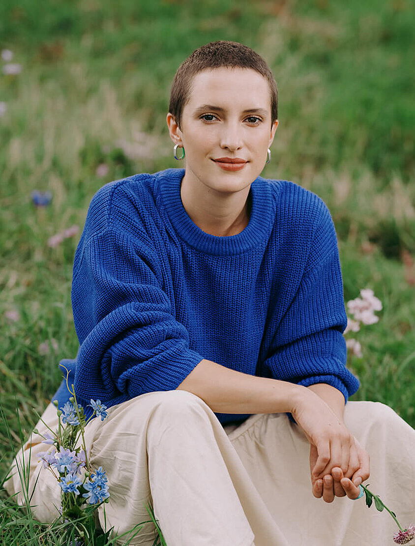 Junge Dame mit kurzer Frisur sitzt auf einer Blumenwiese und steht für die Krebsversicherung.