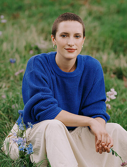 Junge Dame mit kurzer Frisur sitzt auf einer Blumenwiese und steht für die Krebsversicherung.