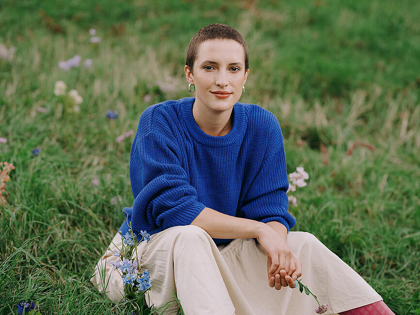 Junge Dame mit kurzer Frisur sitzt auf einer Blumenwiese und steht für die Krebsversicherung.