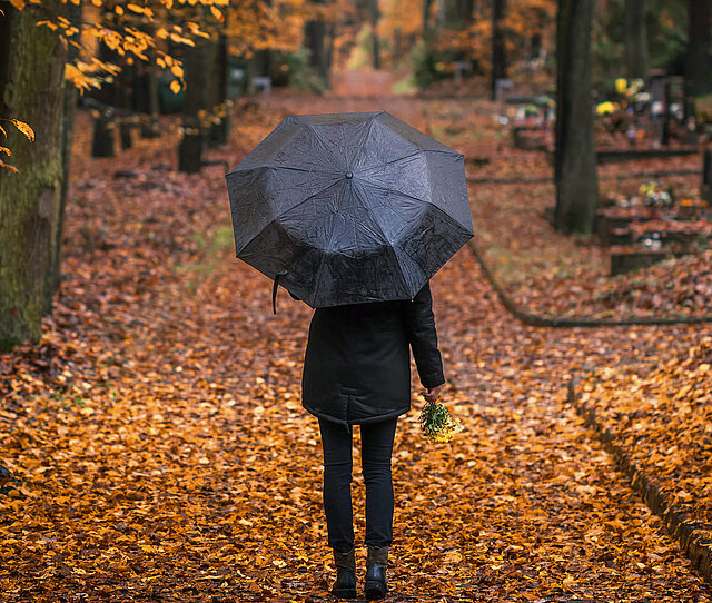 Eine schwarz gekleidete Dame sparziert durch den Wald und denkt über eine Begräbnisvorsorge nach.