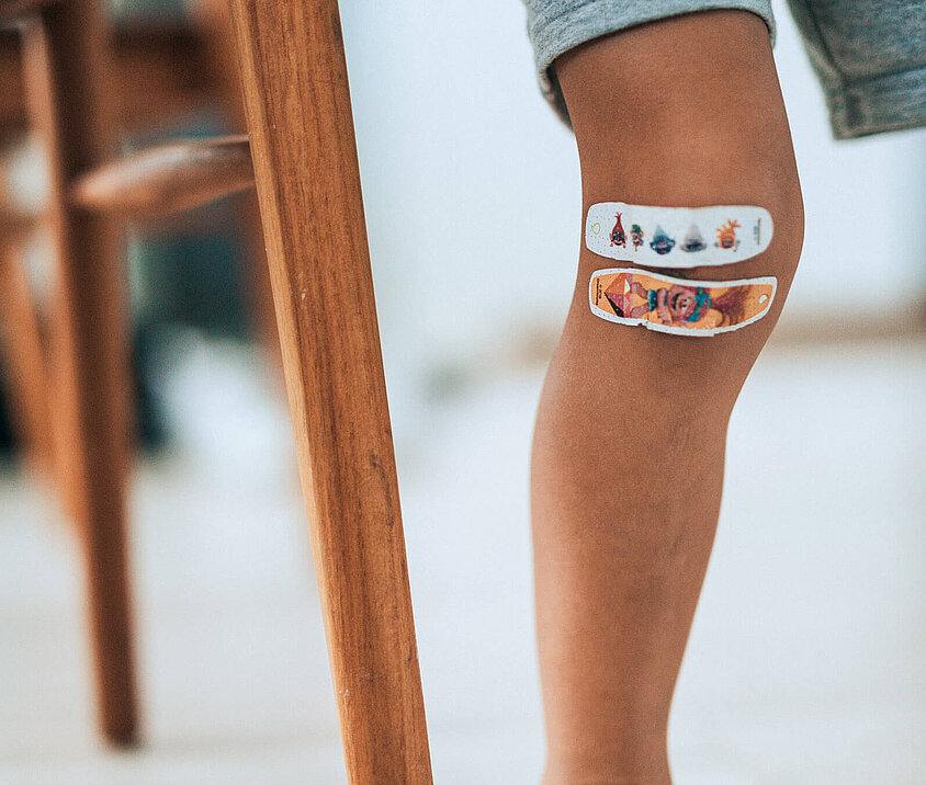 Verletztes Knie eines Kindes mit einem Pflaster, weist auf die DONAU Krankenversicherung für Kinder hin.