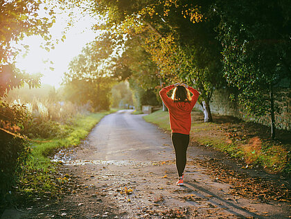 Junge Läuferin in rotem Pullover läuft auf einem Waldweg und macht sich über ihre Gesundheit Gedanken.