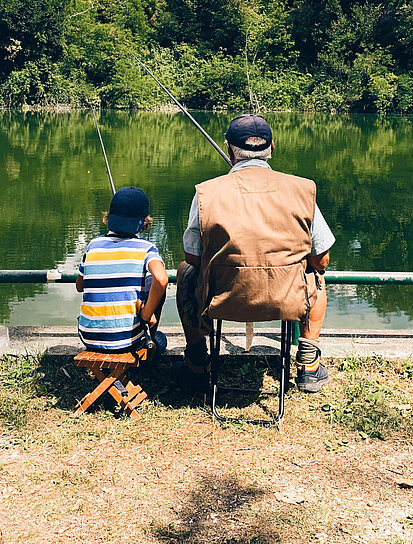Großvater und Enkel angeln im Teich und sprechen über eine Er-  und Ablebensversicherung.