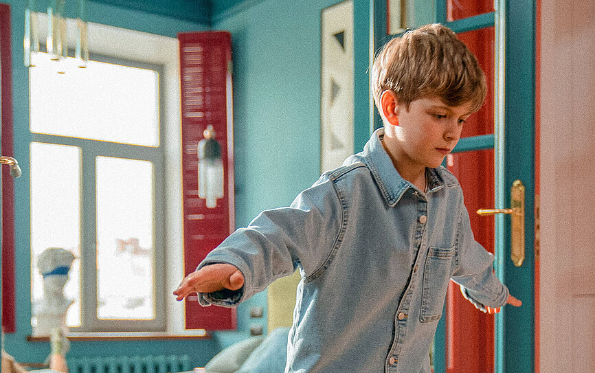 Bruder und Schwester fahren mit dem Skateboard durch die Wohnung und freuen sich, dass ihre Eltern einen Bausparer haben.
