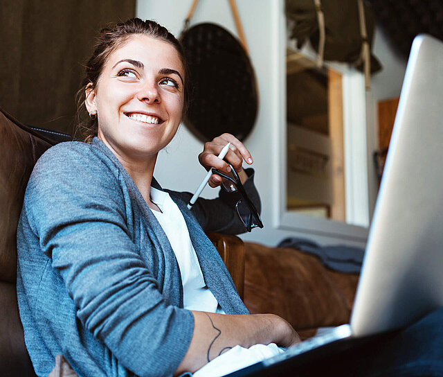 Junge Dame arbeitet am Laptop und steht für die Wohnhausversicherung.