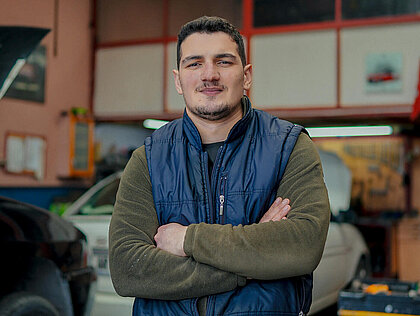 Automechaniker steht vor einem Auto und steht für die Kfz-Versicherung.