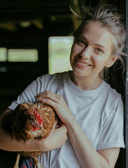 Eine Frau streichelt lächelnd das Huhn in ihrem Arm und möchte ihr Vermögen nachhaltig anlegen.