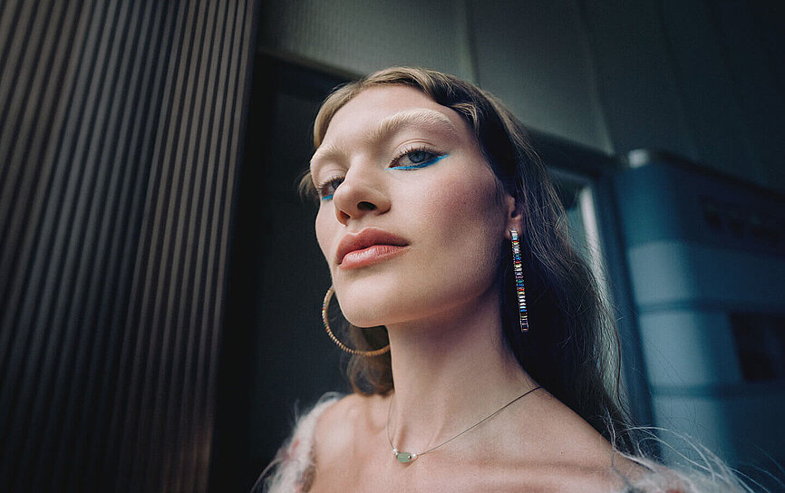 Eine junge Künstlerin mit bunten Ohrringen schaut stolz in die Kamera und ist dankbar für ihre Bonus Pension.