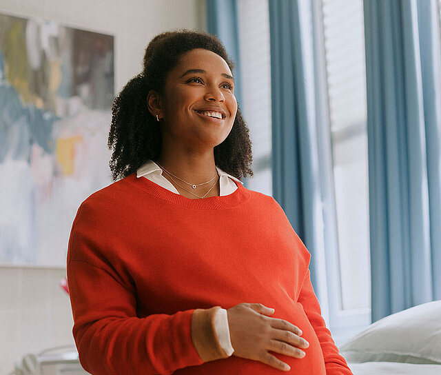 Schwangere Frau in rotem Pullover ist im Krankenhaus und hat eine Sonderklasseversicherung.