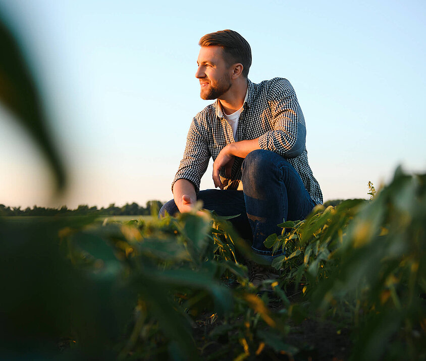 Bauer hockt im Feld und überlegt ob eine Landwirtschaftsversicherung für ihn sinnvoll ist.