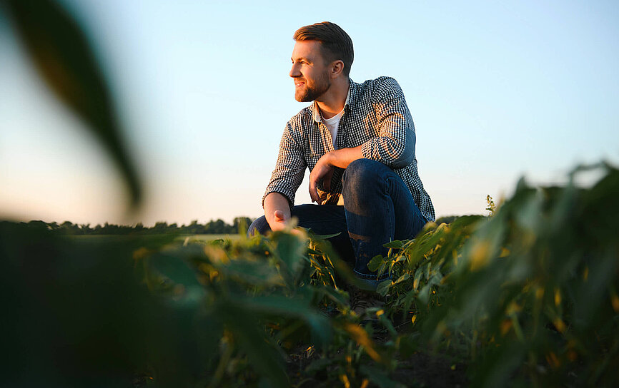 Bauer hockt im Feld und überlegt ob eine Landwirtschaftsversicherung für ihn sinnvoll ist.