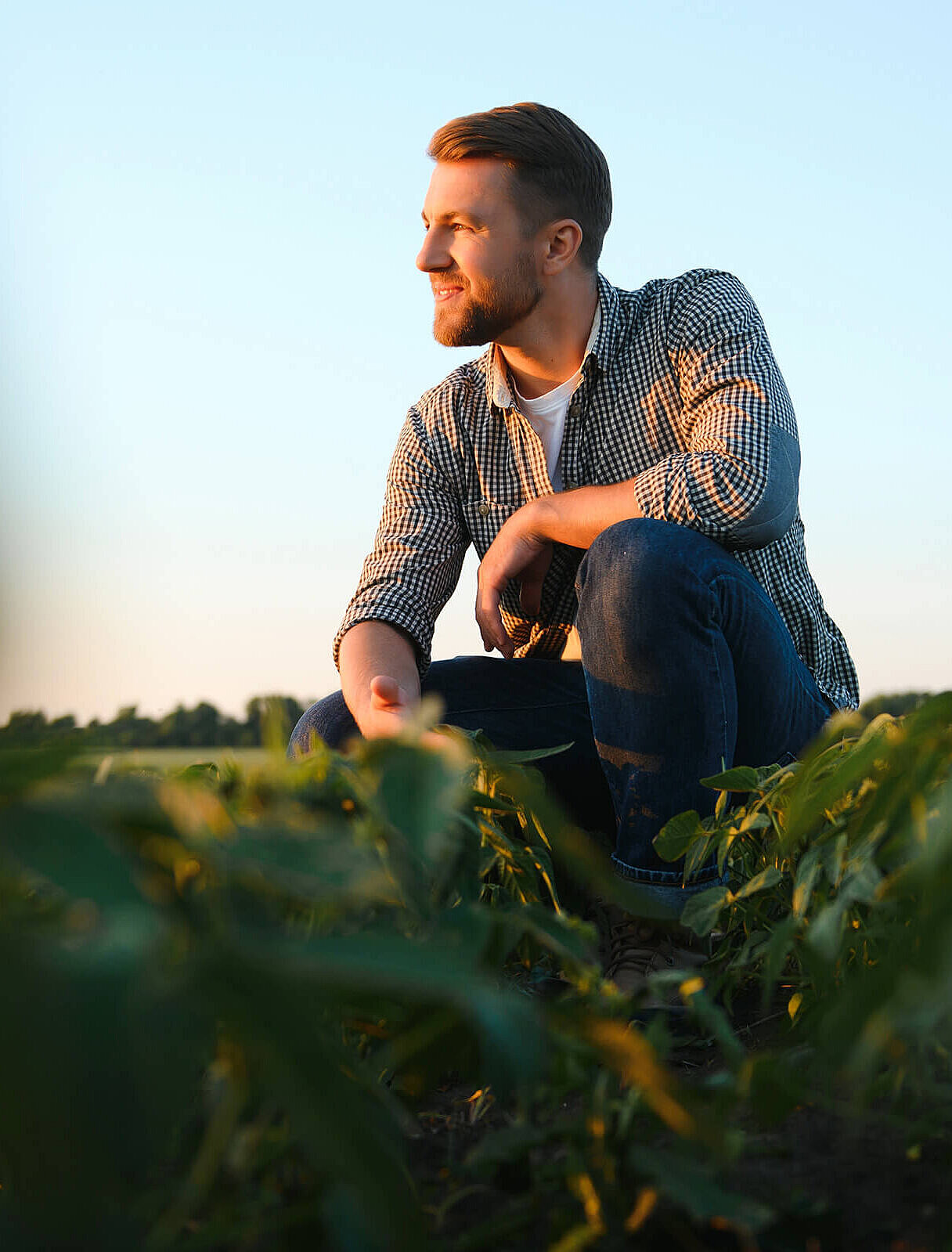 Bauer hockt im Feld und überlegt ob eine Landwirtschaftsversicherung für ihn sinnvoll ist.
