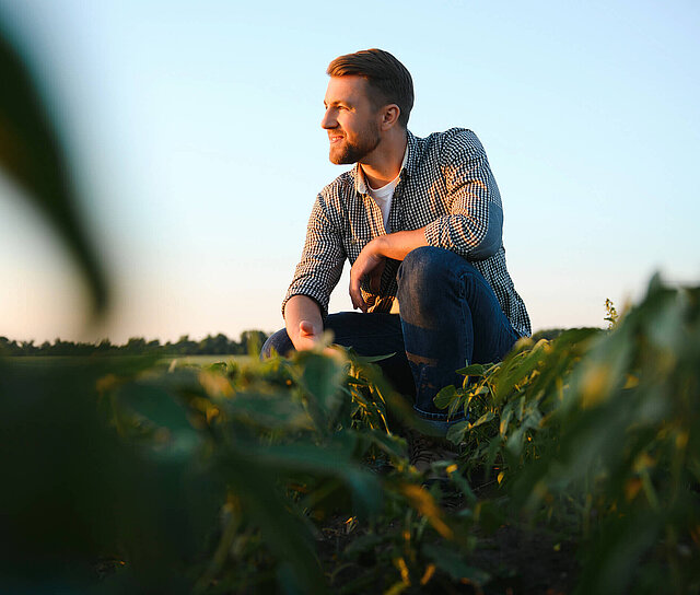 Bauer hockt im Feld und überlegt ob eine Landwirtschaftsversicherung für ihn sinnvoll ist.