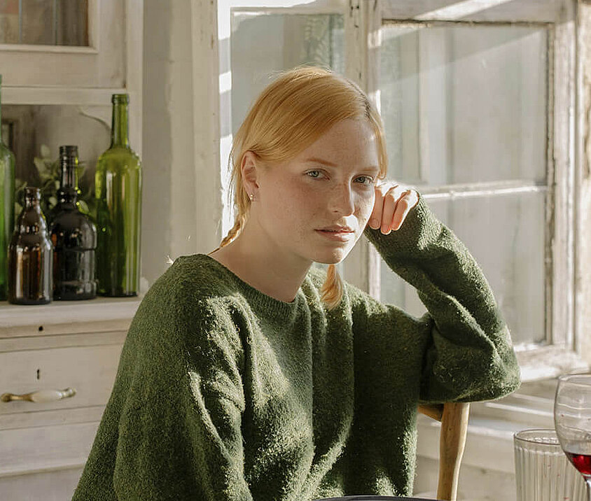 Person in heller Küche am Frühstückstisch, Sonnenlicht fällt durch das Fenster. 