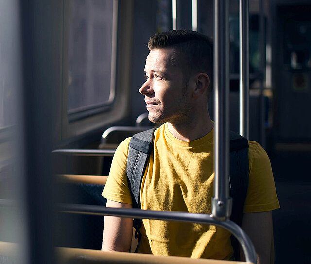 Junger Mann sitzt im Bus, sieht aus dem Fenster und wünschte er hätte eine Berufsunfähigkeitsversicherung.