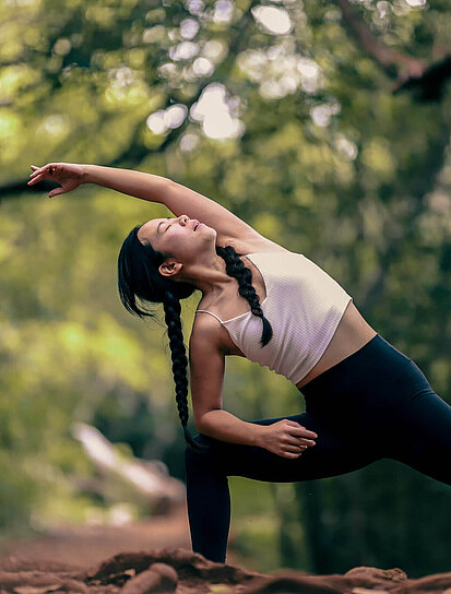 Junge Dame macht Yoga in der Natur und überlegt sich ein Zusatzgesundheitspaket zu holen.