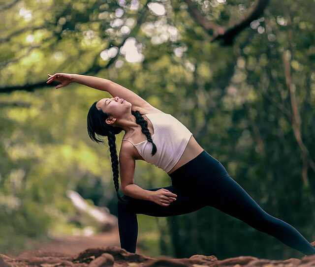 Junge Dame macht Yoga in der Natur und überlegt sich ein Zusatzgesundheitspaket zu holen.