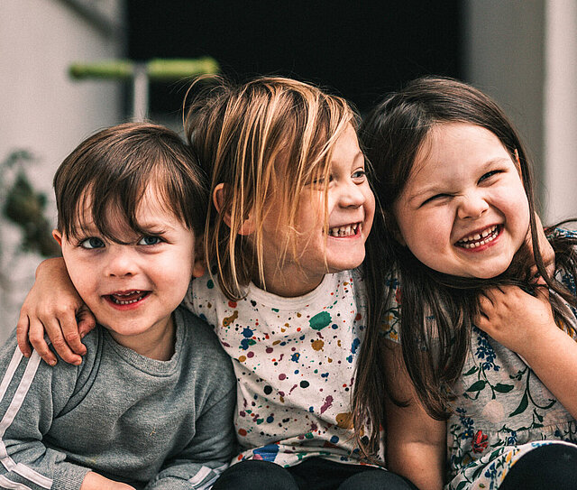 Drei Kinder grinsen in die Kamera und stehen für DONAU for Kids.