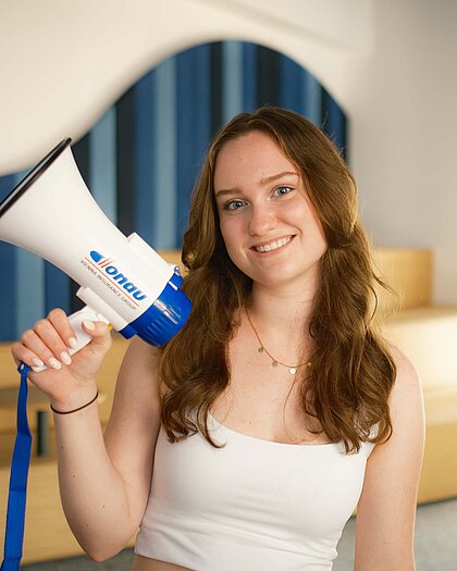 Eine junge Frau hält ein Megafon mit einem DONAU Logo in modernen Büroräumen.