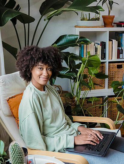 Frau sitzt mit ihrem Laptop auf einem Stuhl im Wohnzimmer und informiert sich zur Cyberversicherung der DONAU. 