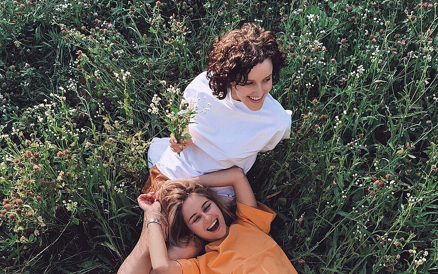 Zwei junge Mädchen sitzen in der Blumenwiese und überlegen wie sie ihr Vermögen anlegen können.