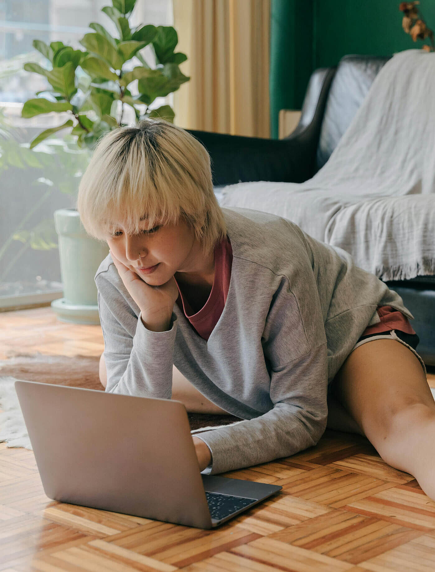 Blonde Frau sitzt mit Laptop im Wohnzimmer und denkt über eine Cyberversicherung nach. 