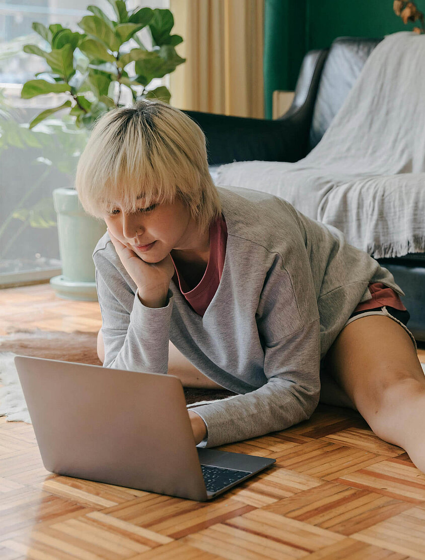 Blonde Frau sitzt mit Laptop im Wohnzimmer und denkt über eine Cyberversicherung nach. 