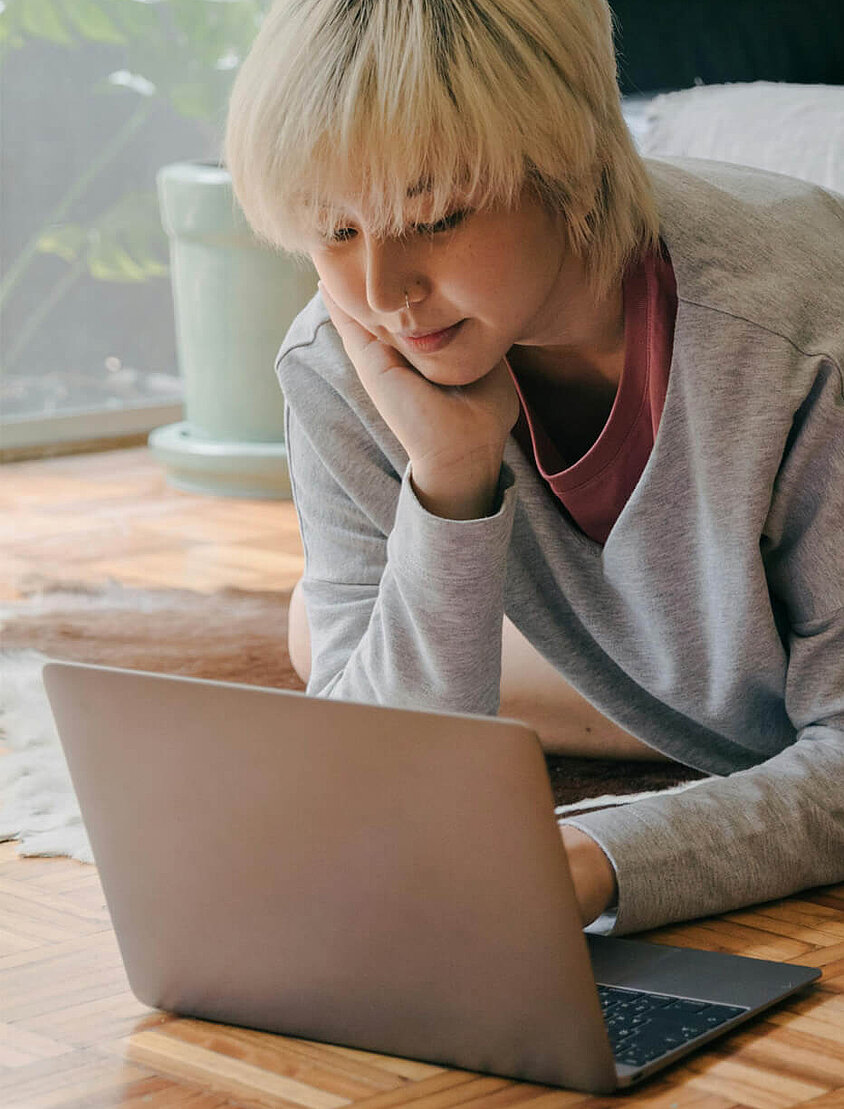 Blonde Frau sitzt mit Laptop im Wohnzimmer und denkt über eine Cyberversicherung nach. 
